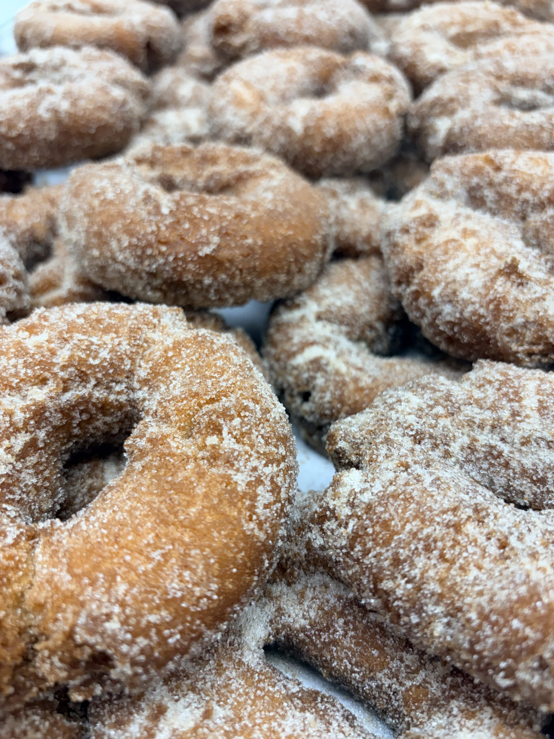 Close-up of sugar-dusted doughnut holes in a pile, showing crispy golden-brown surfaces.